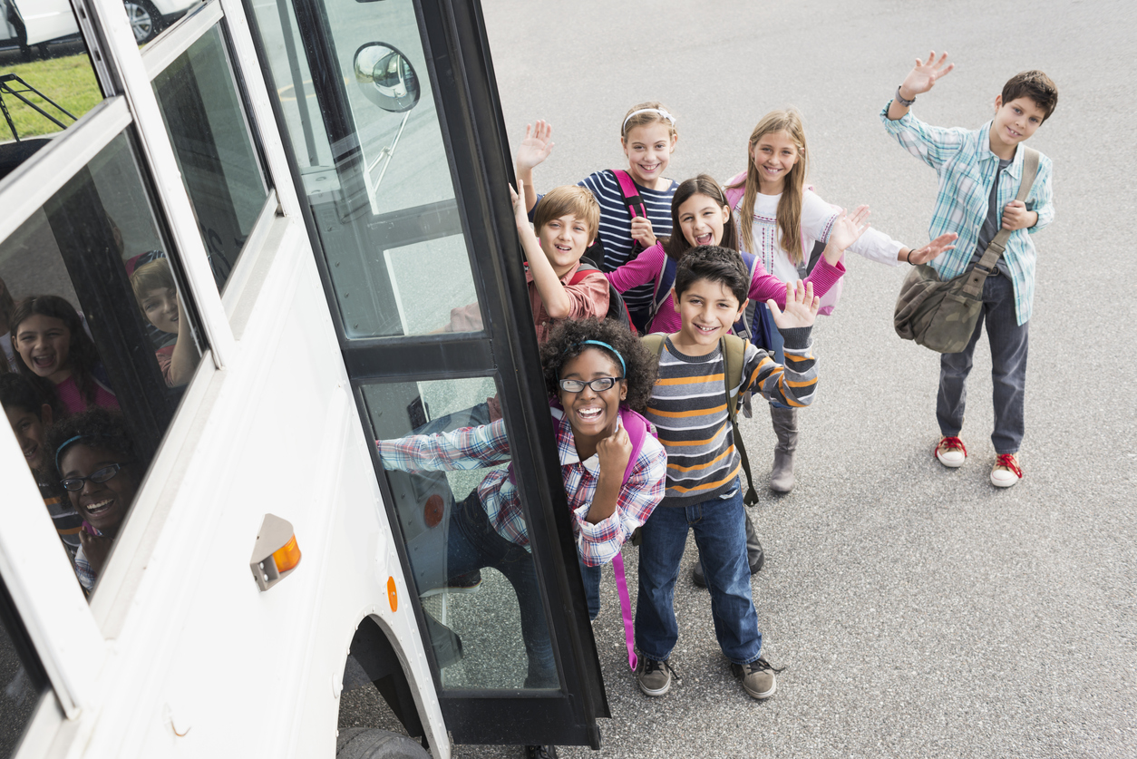 Children waving as they board a school bus